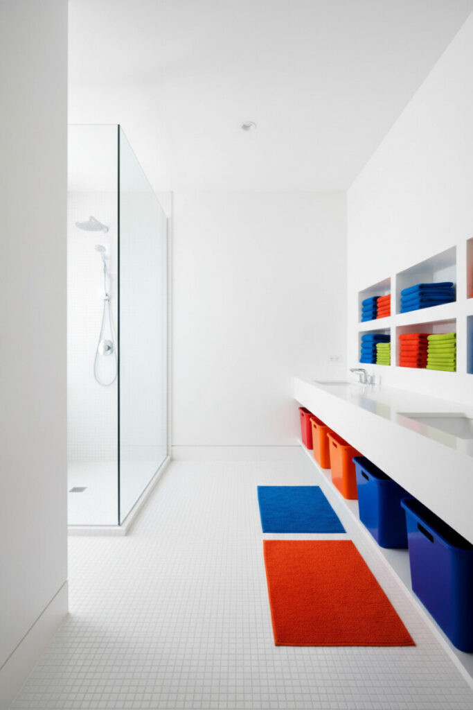 All-white narrow bath with frameless shower, floating counter and bright bins—color-coded storage, small boys bathroom ideas, Boys Bathroom Designs.