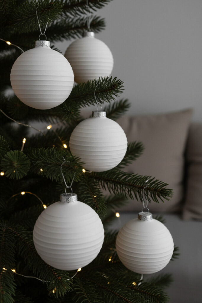Close-up of four matte white fluted ornaments glowing over deep green needles and fairy lights—scandinavian modern Christmas ideas translated into lantern-like baubles.