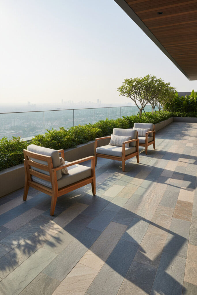 Spacious patio of large stone tiles with three teak armchairs and dense perimeter foliage overlooking hazy skyline—elegant urban terrace design.